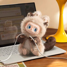 Load image into Gallery viewer, A small plush monkey toy with large blue eyes, a fluffy cream and brown costume, and a long tail sits on a laptop keyboard in a warm indoor setting. A yellow lamp is visible in the background, along with a white cable draped across the scene.

