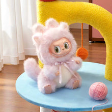 Load image into Gallery viewer, A plush toy doll with a fluffy pale pink animal-like hood and a white belly sits on a light blue round table in a bright indoor room. A yellow cat tree arch is behind it, with a pink yarn ball on the table and a wooden floor nearby.
