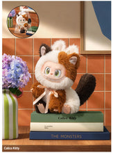 Load image into Gallery viewer, A Calico Kitty plush toy with large green eyes, sitting on a stack of three books on a wooden shelf. The background features a terracotta tiled wall and a vase of purple flowers.
