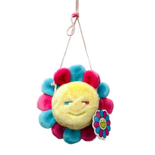 Load image into Gallery viewer, A plush sun-face hanging ornament with a flower-like ruffled border in pink, blue, and yellow, displayed on a glass shelf in a store. Other plush toys are blurred in the background.
