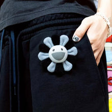 Load image into Gallery viewer, Black jacket with a smiley face design on the pocket, held by a person.
