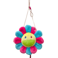 Load image into Gallery viewer, A plush flower-shaped bag or pouch with a yellow face, green mouth, and pink and blue petals, hanging in front of a glass display case with collectible figures in the background.
