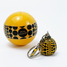 Load image into Gallery viewer, A yellow spherical container with black polka dots and the text 'YAYOI KUSAMA' on the front, shown next to a matching small yellow-and-black polka dot keychain on a white background.

